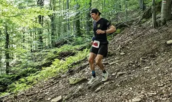 Zawodnik biegnący technicznym, stromym szlakiem w gęstym lesie.