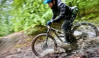 Zawodnik MTB jadący dynamicznie po mokrym, błotnistym szlaku w lesie